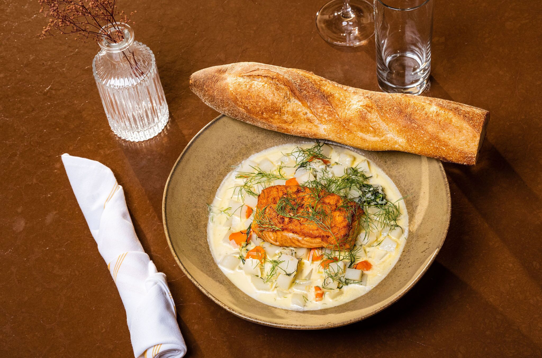 A plate of food with a piece of fish, vegetables, and a baguette on a table.