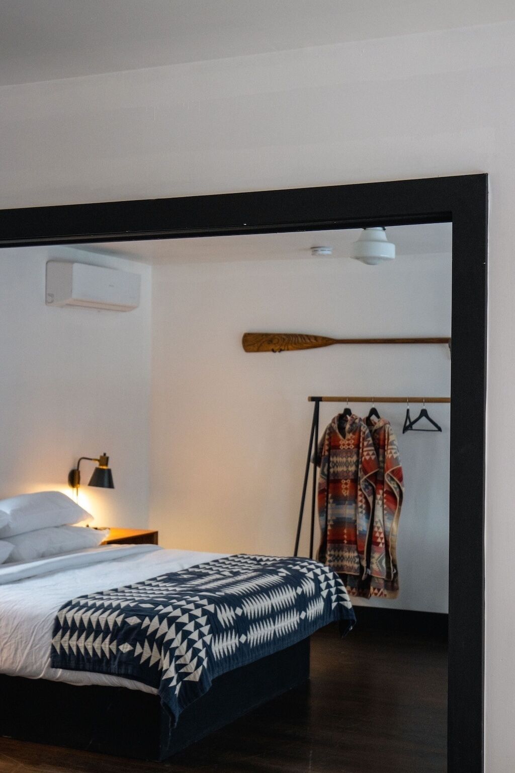 Ein Schlafzimmer mit einem Bett, einer Nachttischlampe, einem Holzschläger und einem Kleiderständer mit Bademänteln.