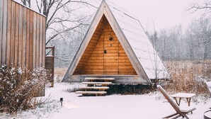 A wooden cabin with a triangular roof, a wooden door, and a bench outside.