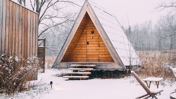 A wooden cabin with a triangular roof, a wooden door, and a bench outside. - Eastwind Windham (Windham)
