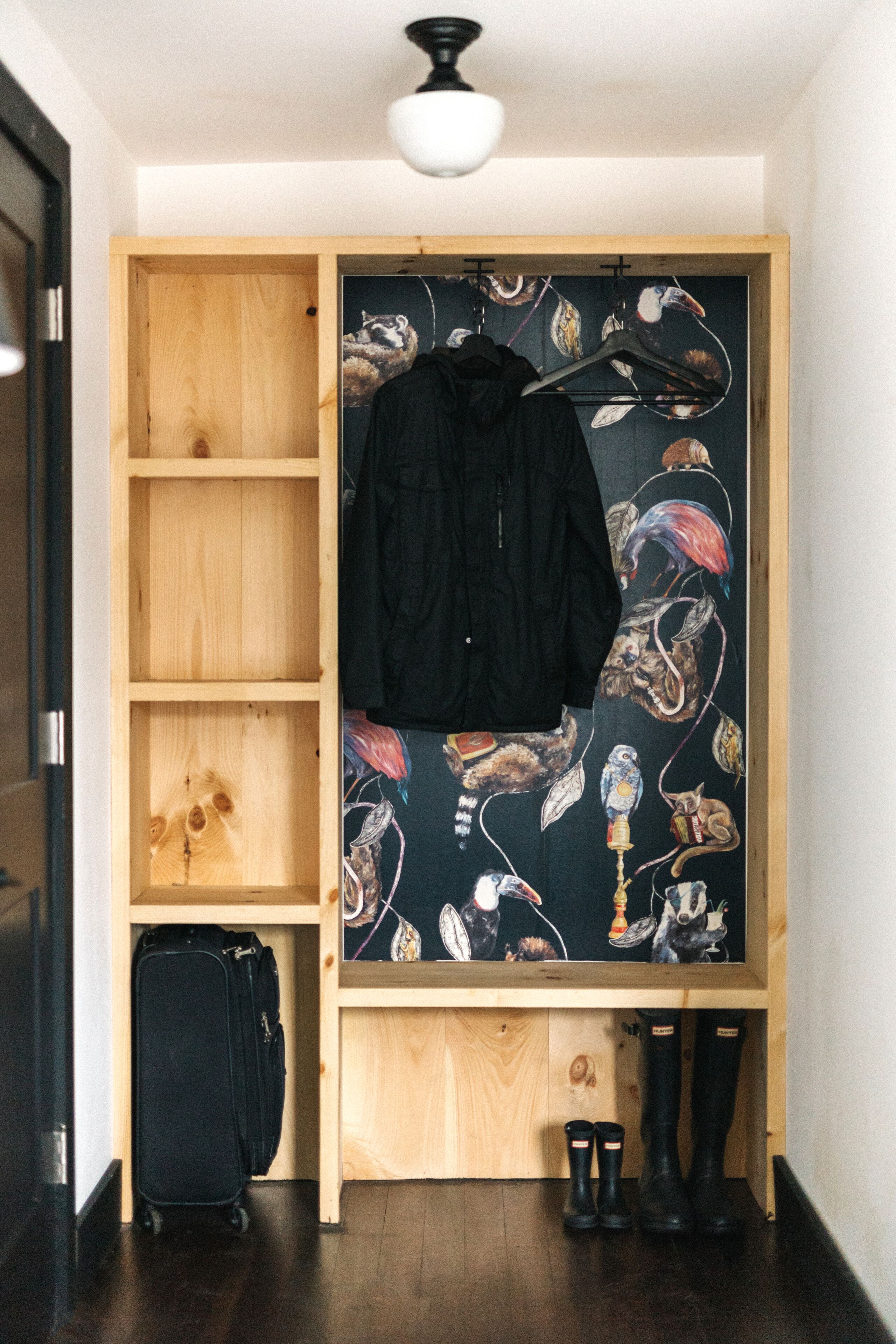 Une petite pièce avec une armoire en bois, un porte-manteau, une valise et des bottes noires.