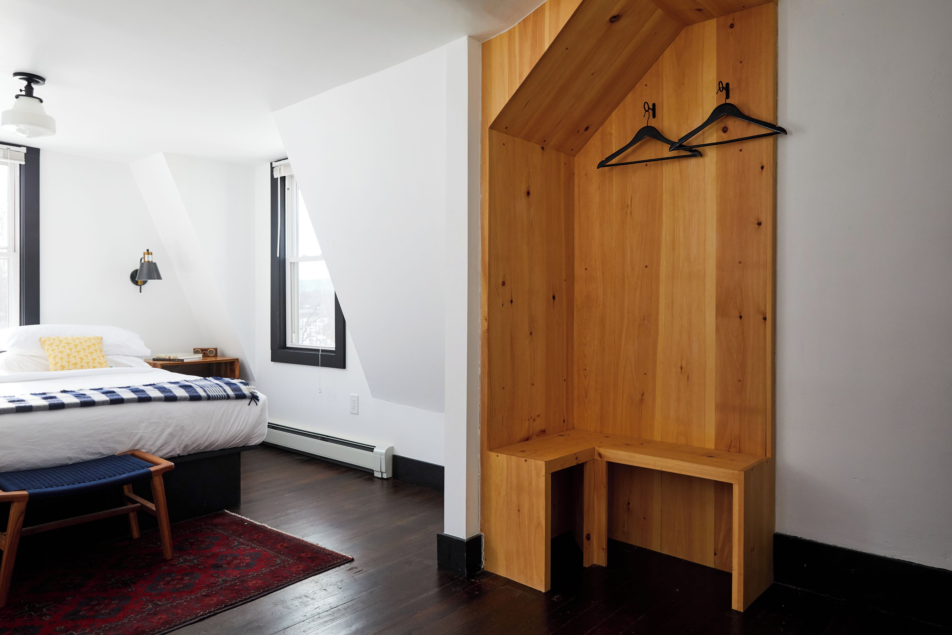 A bedroom with a bed, bench, and wooden wardrobe with hangers.