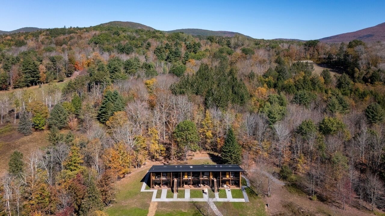 A modern building with a flat roof, surrounded by a forested hillside.