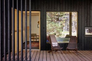 A wooden deck with two chairs and a bench, overlooking a forested area through a large window.