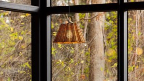 A round wooden table with a hanging light fixture, surrounded by four stools, set against a backdrop of a large window with a view of trees and a wooden deck. - Eastwind Windham (Windham)