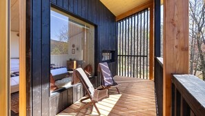 A wooden deck with two lounge chairs and a small table, overlooking a forested area.