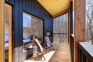 A wooden deck with two lounge chairs and a small table, overlooking a forested area.