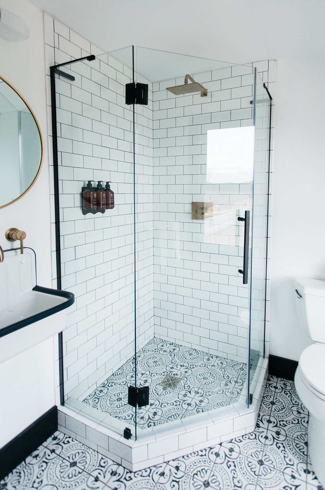 A glass-enclosed shower with white and black patterned tiles, a black countertop, and a white toilet.