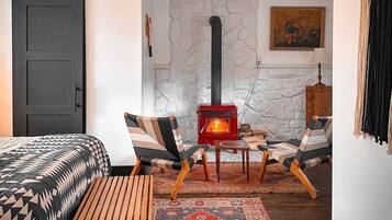 Una habitación acogedora con una cama, un banco de madera, un estufa de leña roja y una alfombra estampada.