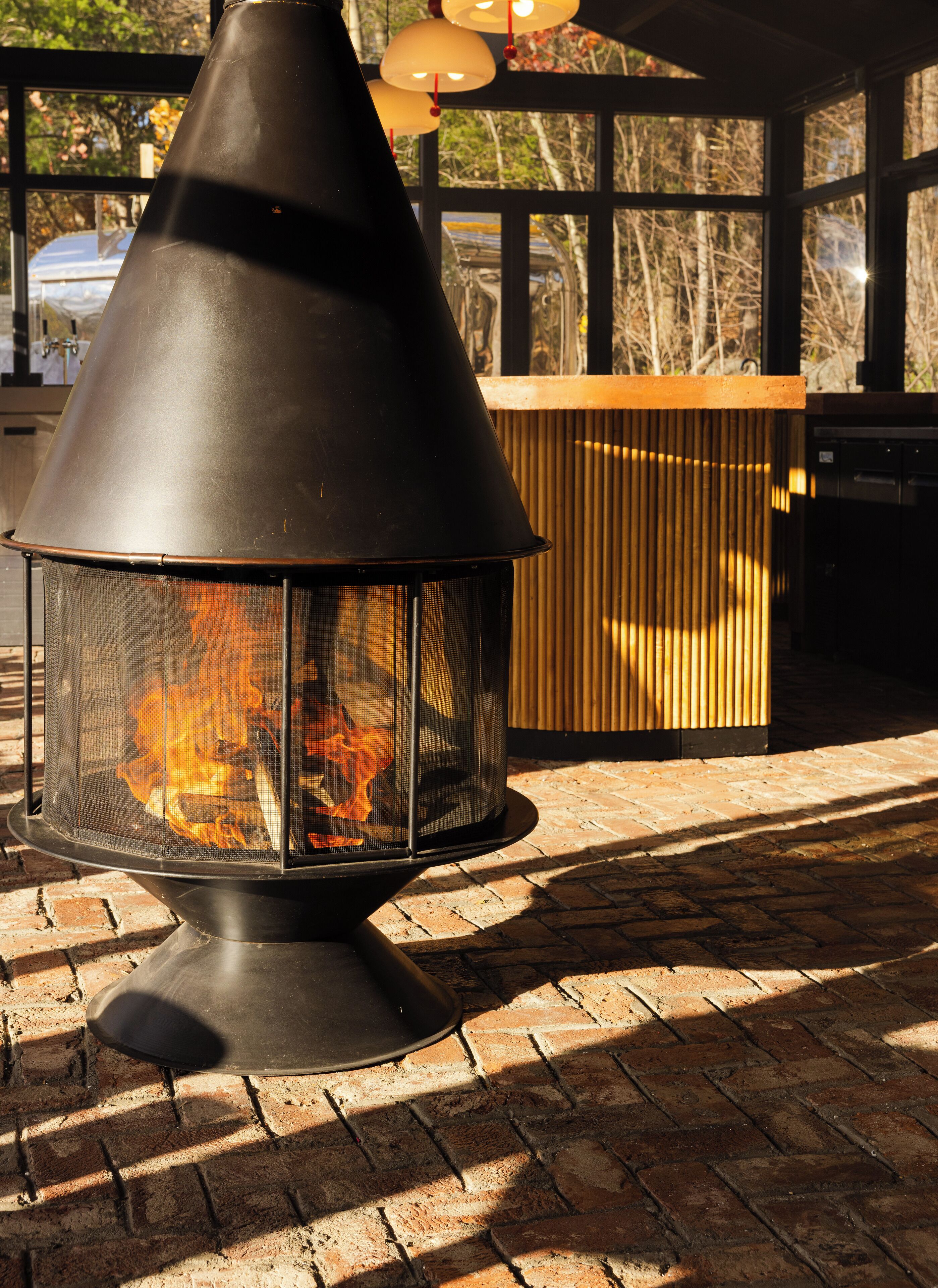 A black outdoor fire pit with a mesh screen, surrounded by a brick patio.