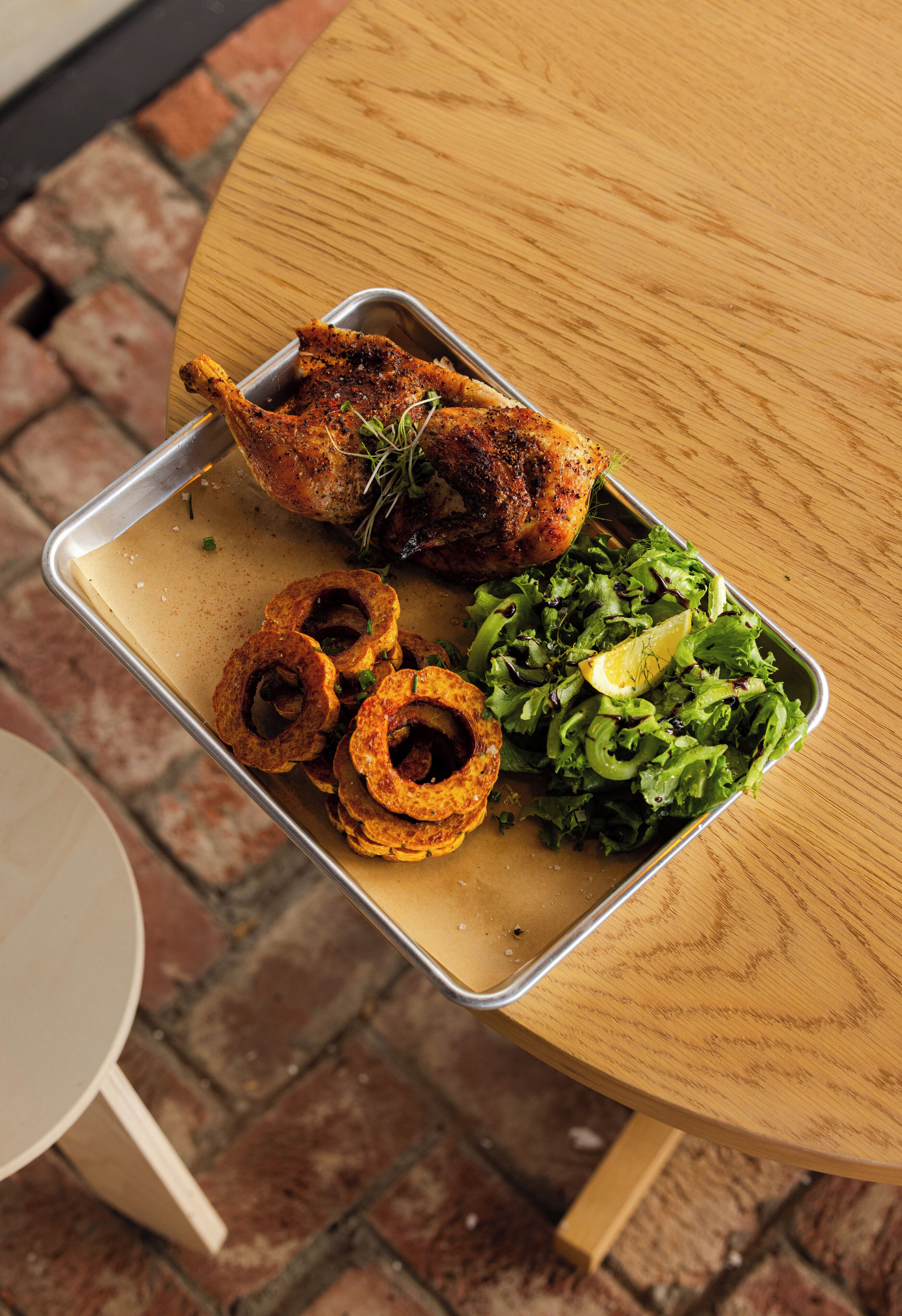 Una comida con pollo asado, aros de cebolla y una ensalada verde sobre una bandeja metálica.