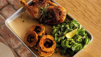 Una comida con pollo asado, aros de cebolla y una ensalada verde sobre una bandeja metálica.