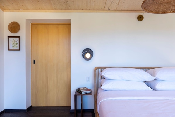 A bedroom with a wooden door, a bedside table with a lamp, and a bed with white bedding.
