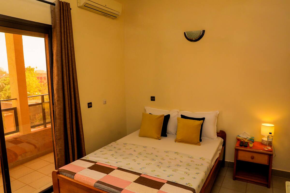 Una habitación de hotel con una cama, una mesita de noche, una lámpara y vistas al exterior.