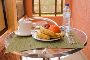A table with a plate of fruit, a glass of water, a cup, and cutlery. - AG HOTEL Ouaga (Ouagadougou)