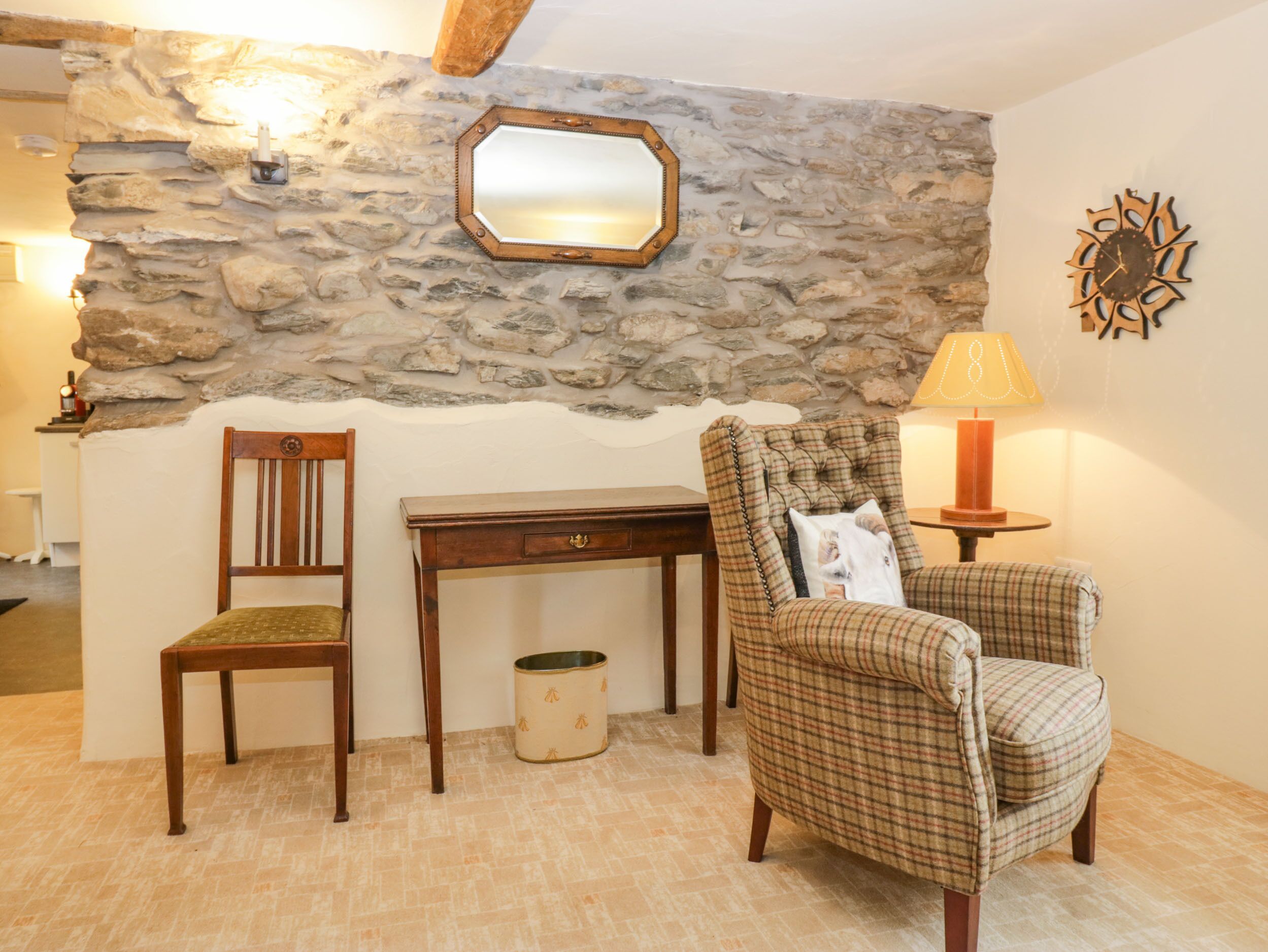 A room with a stone wall, a wooden chair, a small table, a lamp, and a mirror.