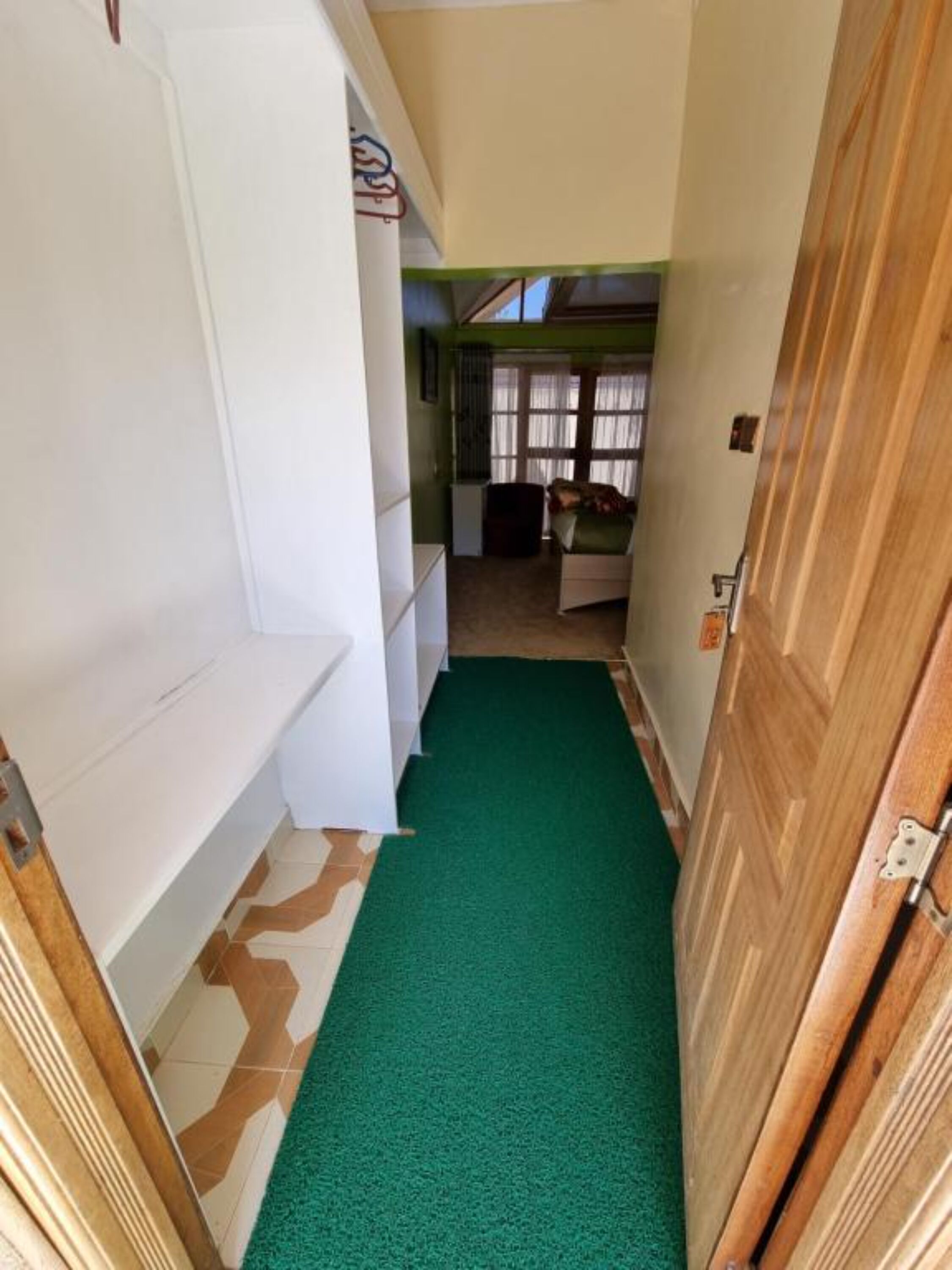 A narrow hallway with a green carpet, white walls, and a wooden door.