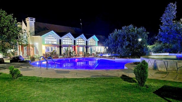 A well-lit swimming pool area with a house in the background.