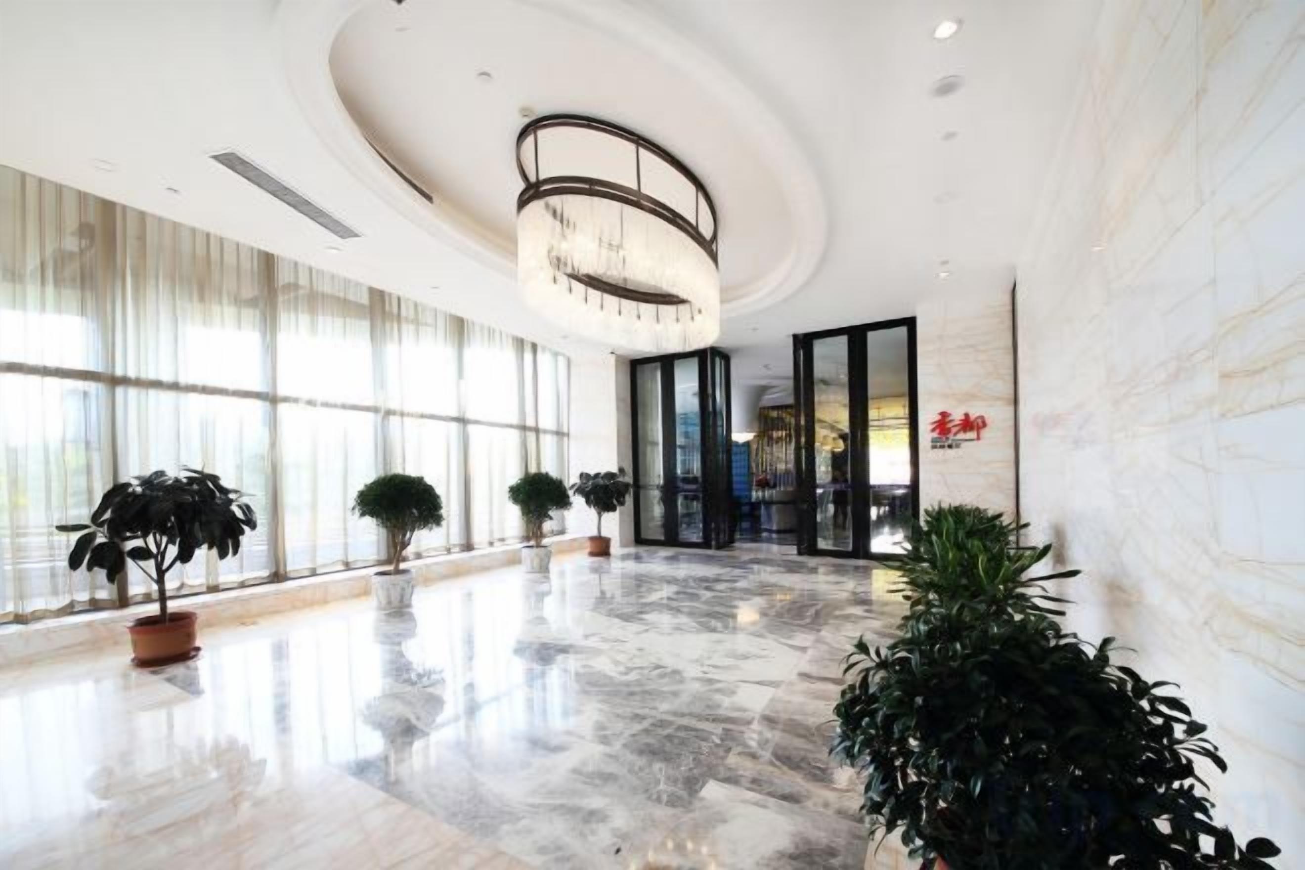 A spacious lobby with a marble floor, large windows, and potted plants.