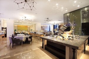 Un amplio hall de hotel con zona de comedor central, diversas opciones de asientos y un espejo grande que refleja el salón.
