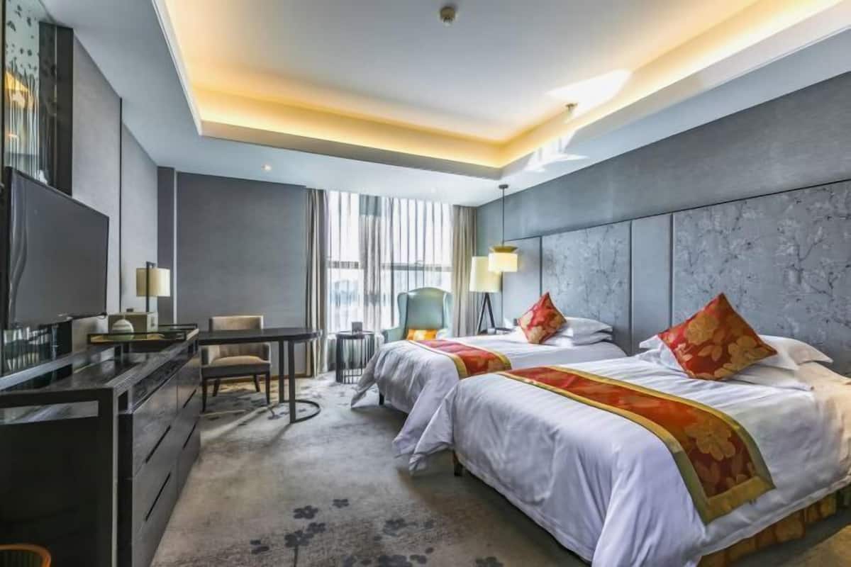 A modern hotel room with two beds, a desk, a chair, and a television.