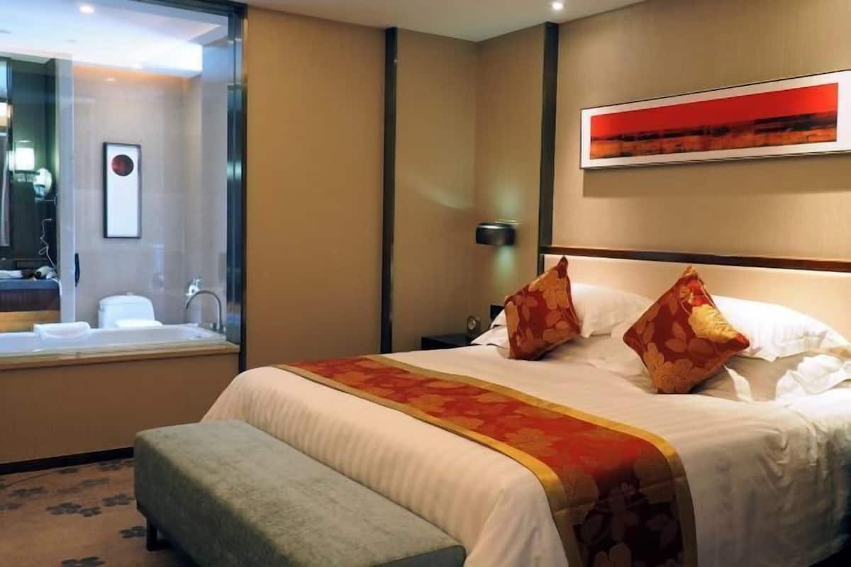 A hotel room with a large bed, a bedside table, a mirror, a window, and a wall-mounted artwork.