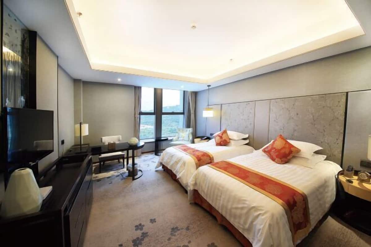 A hotel room with two beds, a desk, a TV, and a large window.