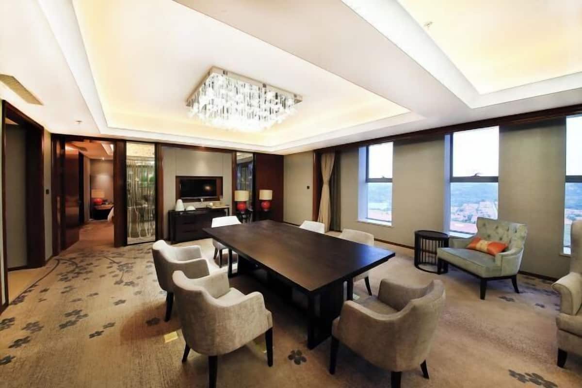 A modern hotel room with a large dining table, comfortable seating, a television, and a view of the city.