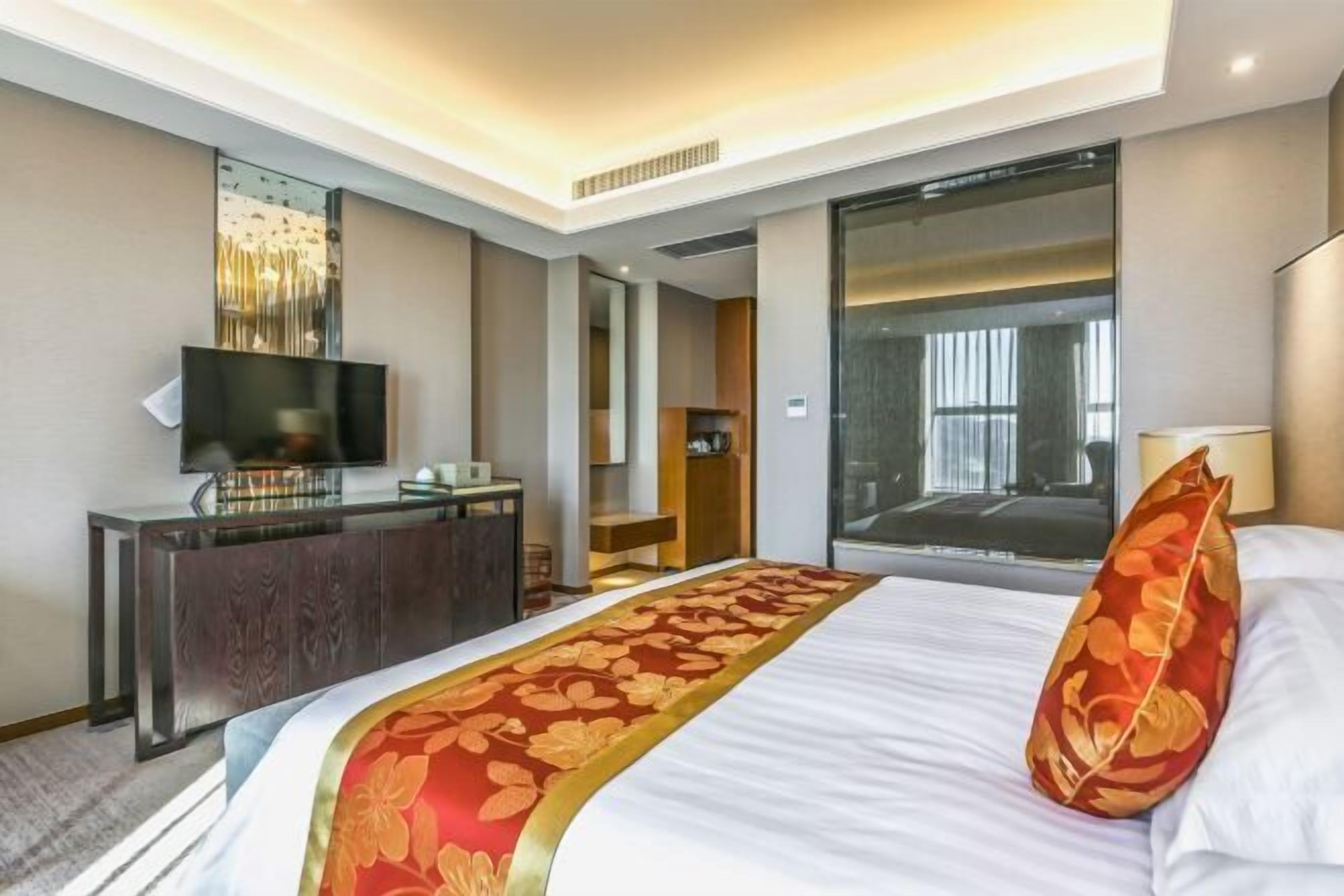 A hotel room with a bed, a TV, a desk, and a large window.