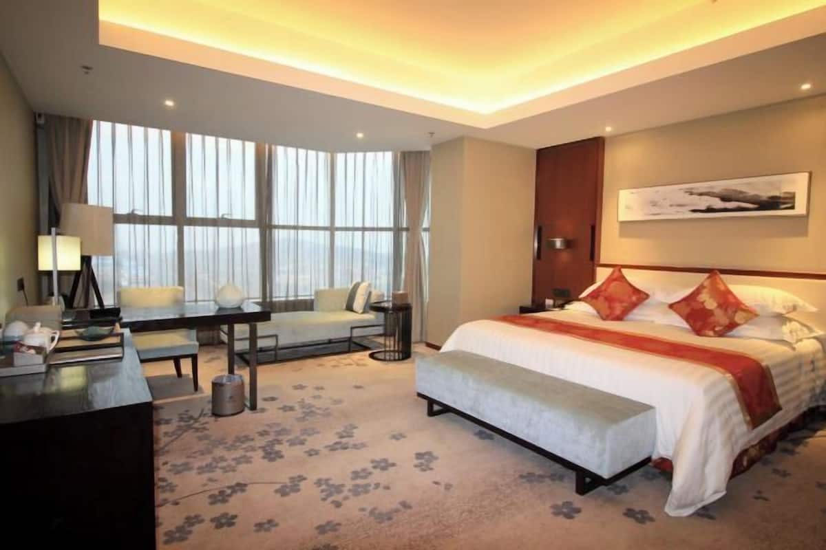 A hotel room with a large bed, a desk, a sofa, and a view of the city.