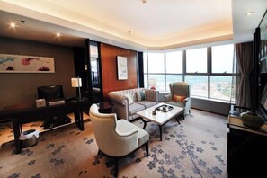 A hotel room with a sofa, armchair, coffee table, and a desk with a lamp. - Longhu Hotel (Zhaoyuan)