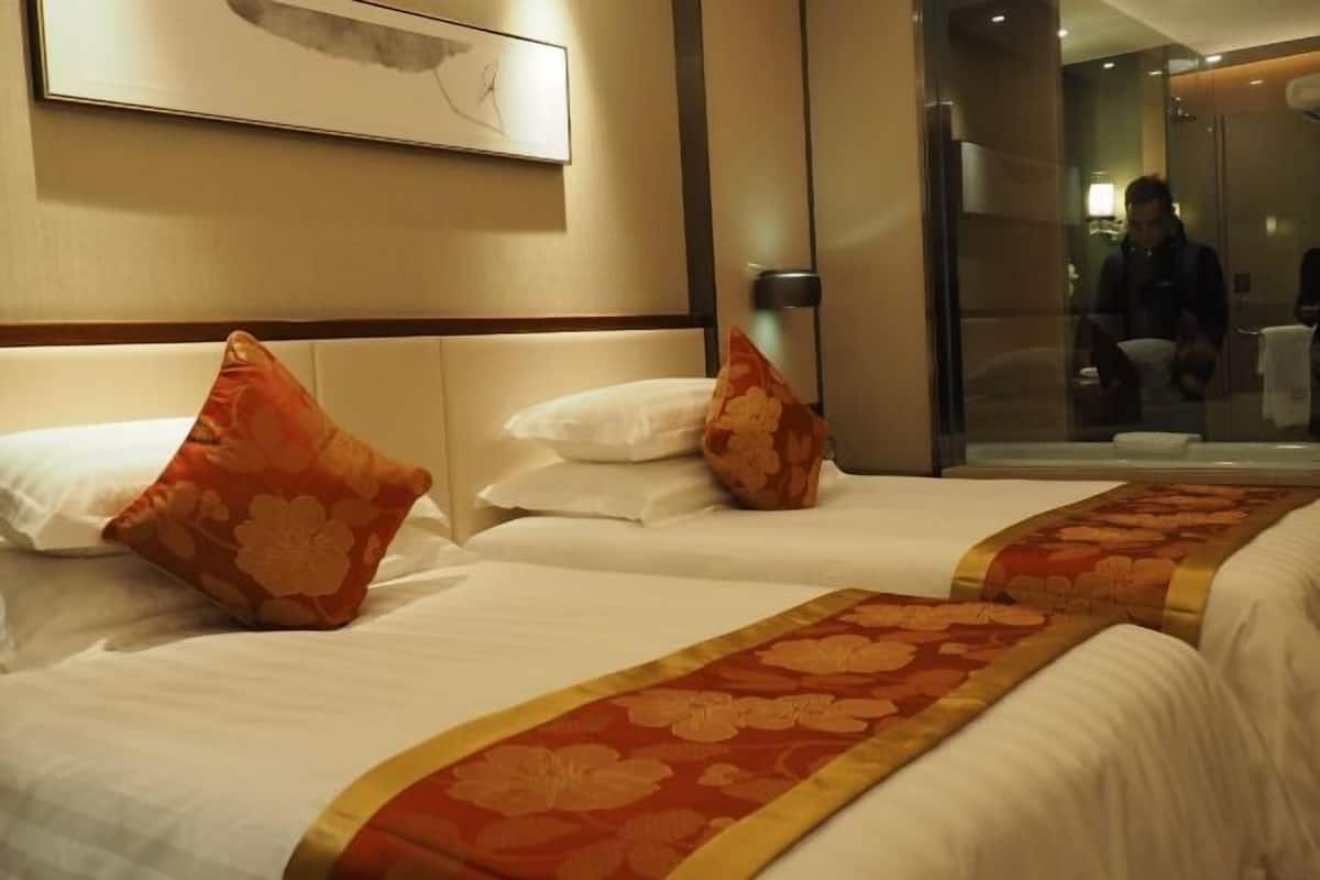 A hotel room with two beds, each with white bedding and orange floral pillows.