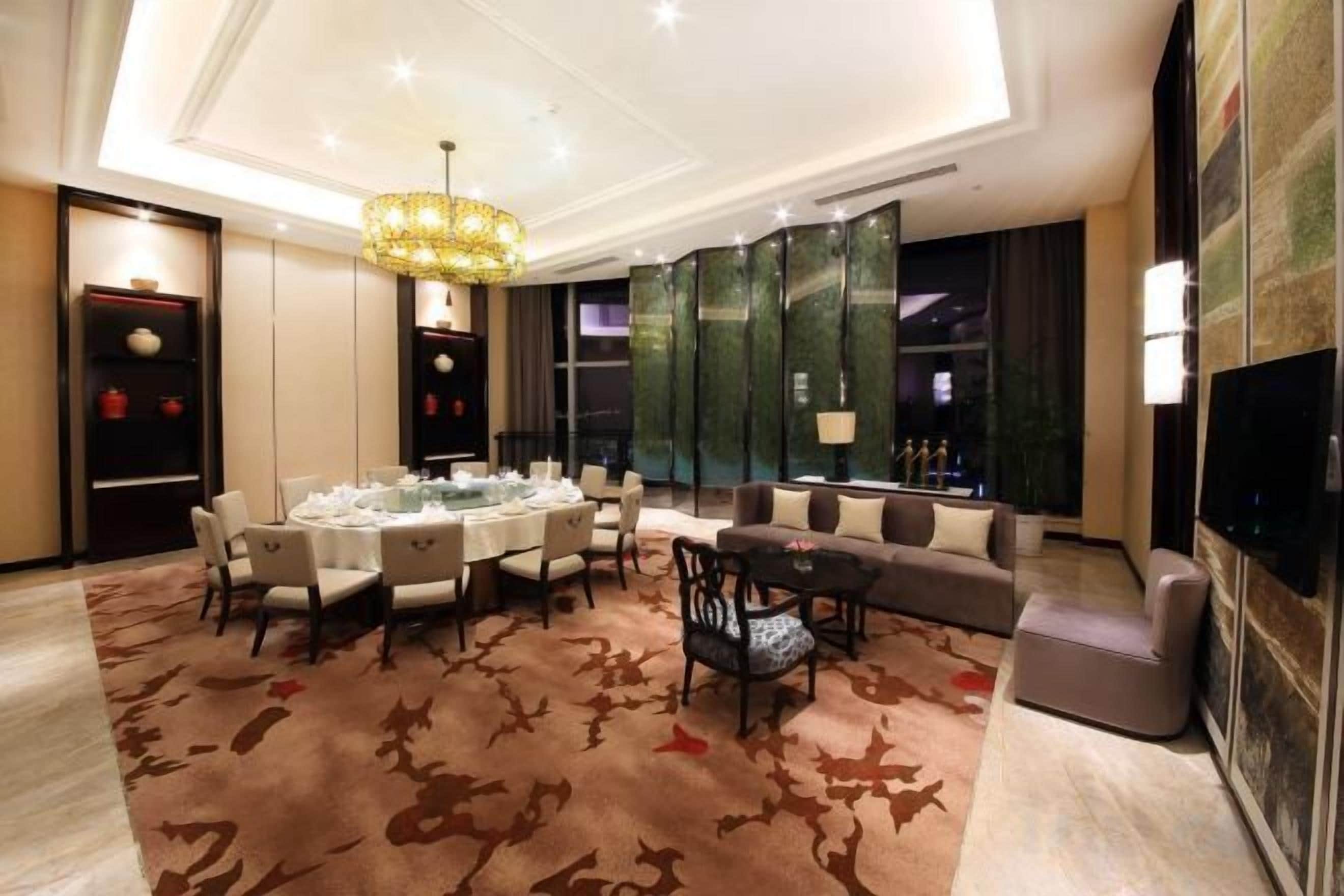 A modern hotel room with a dining area, a sofa, a TV, and a fireplace.