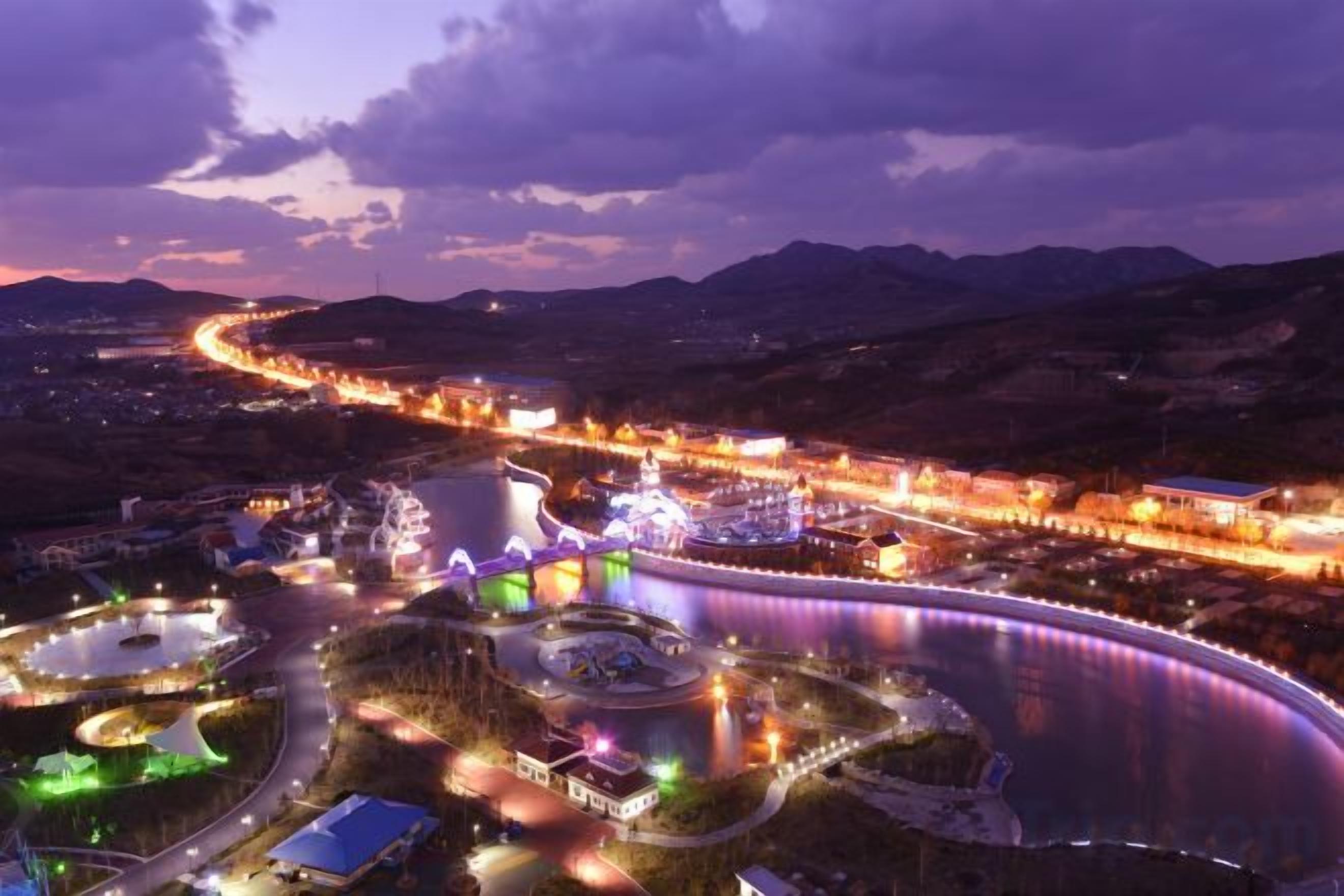 A large, illuminated water body with surrounding buildings and a curved road.