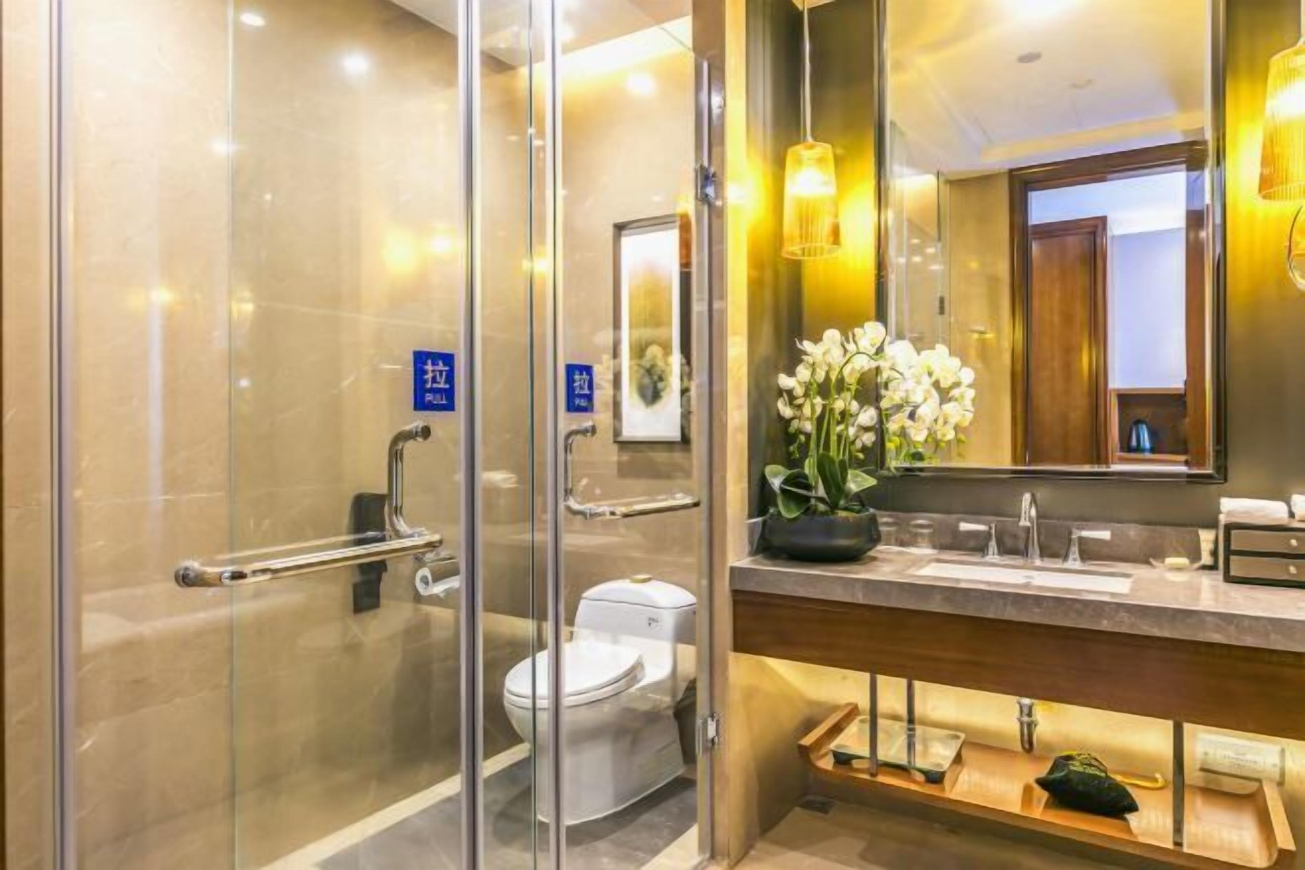 Une salle de bain moderne avec une douche en verre, des toilettes blanches, un lavabo avec un miroir et une orchidée en pot.