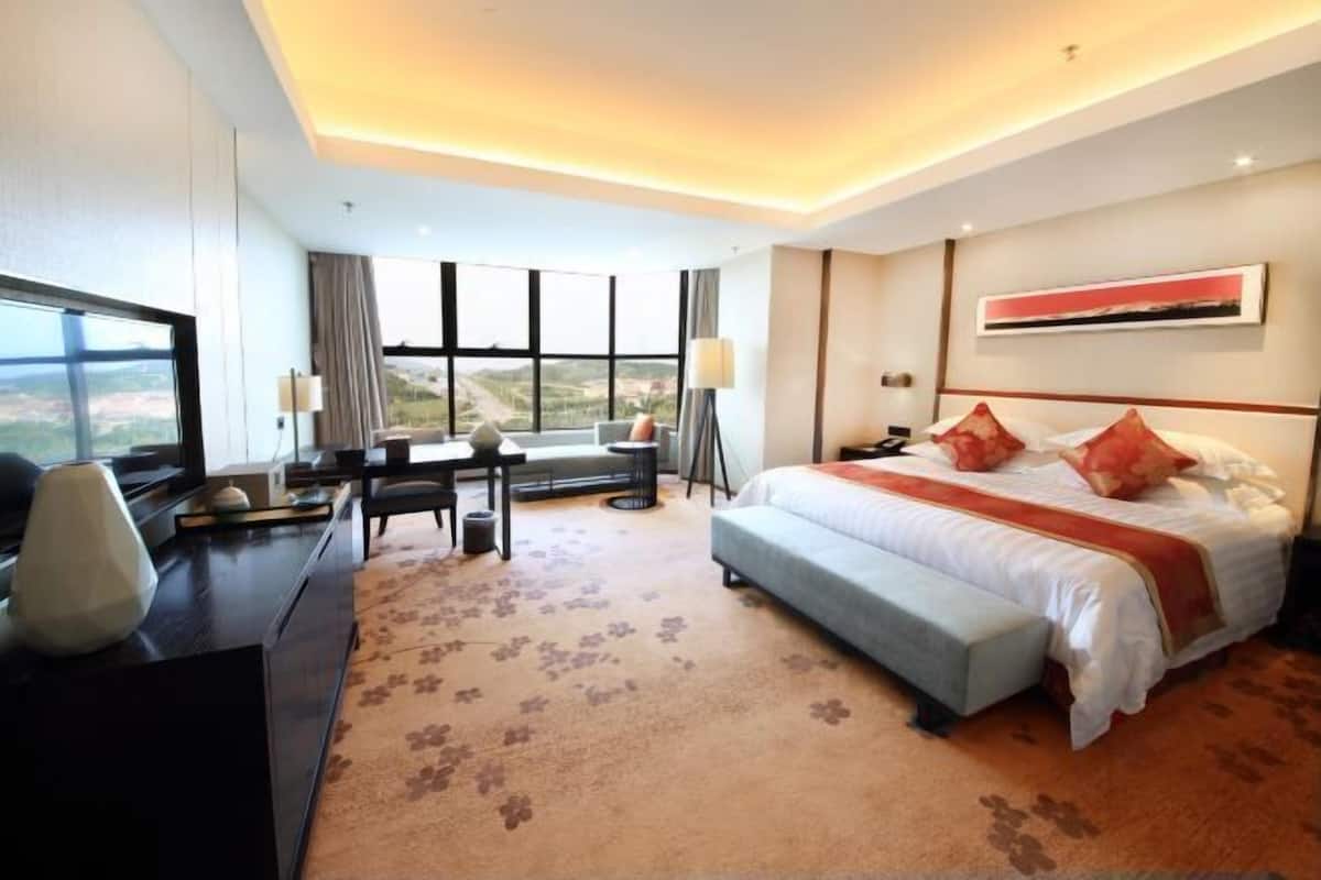 A hotel room with a large bed, a desk, a chair, and a TV.