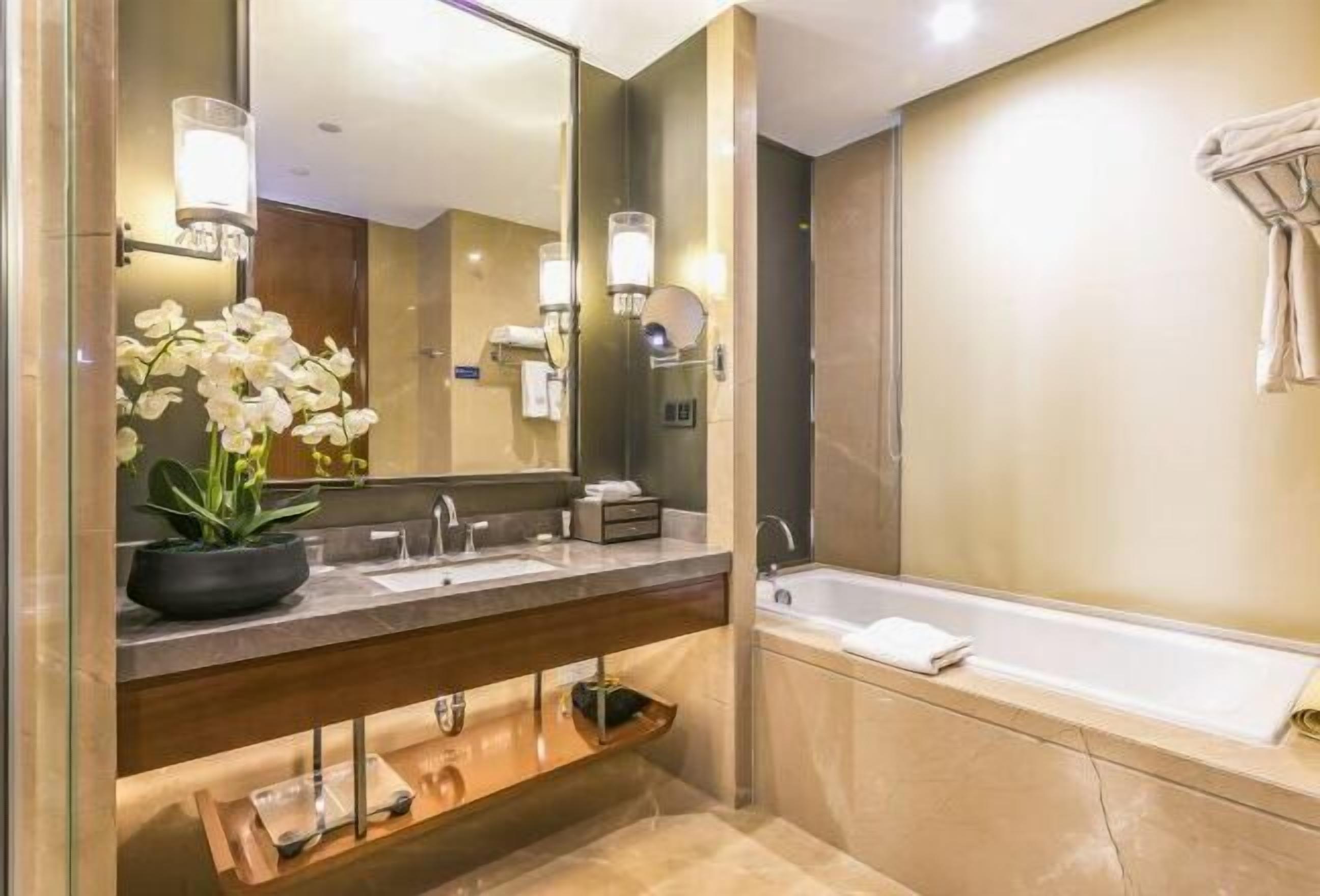 Une salle de bain moderne avec un grand miroir, deux lavabos, une baignoire et une orchidée en pot.