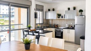 Una cucina moderna con mobili bianchi, un frigorifero in acciaio inossidabile e un'area pranzo con tavolo in legno e sedie bianche.