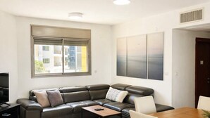 Un soggiorno moderno con un divano ad angolo, un tavolino da caffè, un tavolo da pranzo con sedie, una TV e una finestra con tende.