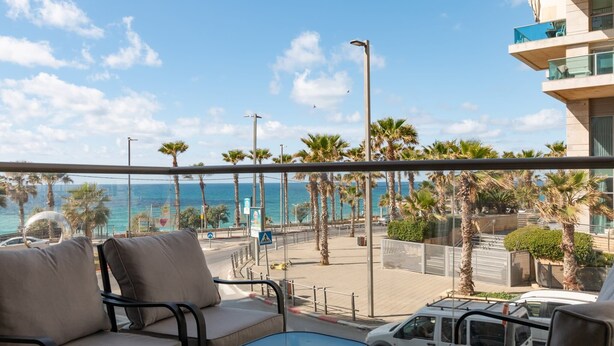 Un balcone con vista sul mare, palme e un edificio con balconi.