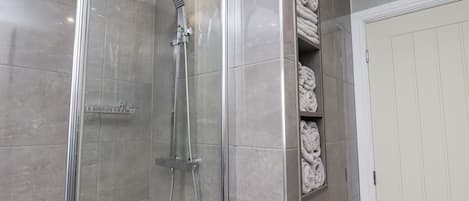 A modern bathroom with a glass-enclosed shower, a built-in towel rack, and a white door.