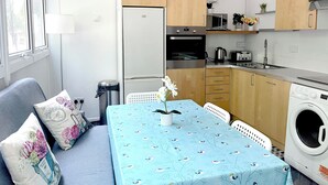 Une cuisine compacte équipée d’un lave-linge, d’une table à manger recouverte d’une nappe bleue et de meubles de rangement en bois.