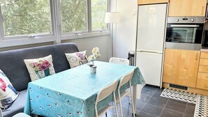 Une cuisine moderne avec un coin repas, comprenant une table recouverte d’une nappe bleue, des chaises blanches et un canapé agrémenté de coussins à motifs.
