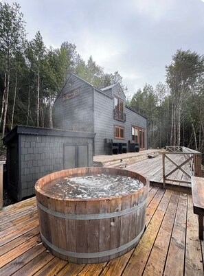 Une cabane dotée d’un bain à remous, d’une terrasse et donnant sur une forêt.