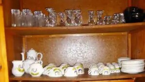 Un buffet en bois, doté de plusieurs étagères, où sont rangés divers plats et services en céramique blanche, notamment des assiettes, des bols et des théières.