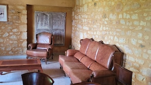 Un salón con pared de piedra, una mesa de centro de madera, un sofá de cuero, un sillón de cuero y un armario de madera.