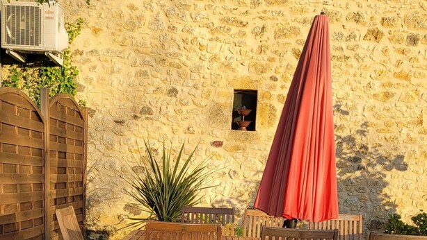 Un patio al aire libre con mobiliario de mimbre, una mesa de madera y un paraguas rojo.