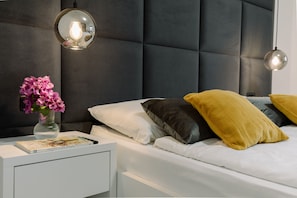 A modern bedroom with a tufted headboard, a bedside table with a book and a vase of flowers, and a bed with white and mustard pillows. - Boutique Suites Joyce Medulin (Medulin)