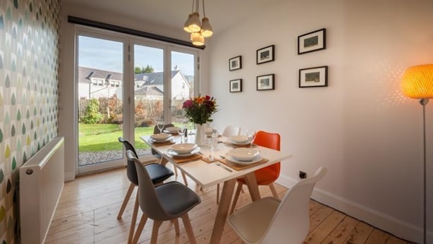 A dining area with a table set for four, chairs, a vase with flowers, and framed pictures on the wall. - Gorgeous Comrie Cottage, hot tub & Mountain Views (Crieff)