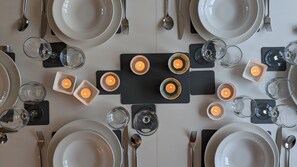 Ein ordentlich gedeckter Tisch mit weißen Tellern, Besteck und Gläsern, in dessen Mitte ein schwarzes Quadrat mit Kerzen steht.